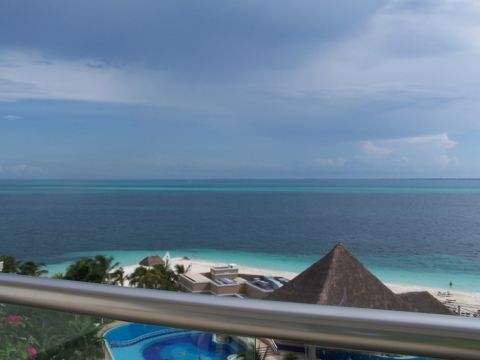 1979 Ford F-150 - A tropical resort overlooks a turquoise ocean and white sand beach under a cloudy sky.