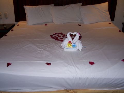 1979 Ford F-150 - A bed is prepared with white linens, scattered rose petals, and two towel swans arranged in a heart shape.