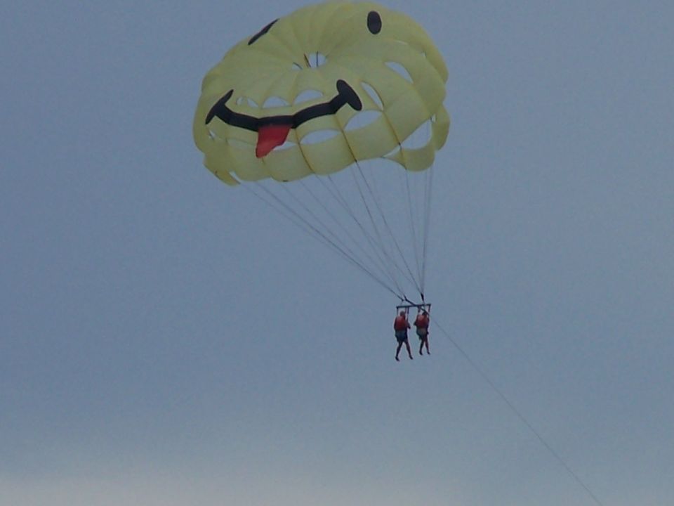Yellow parasail with a smiley face and tongue sticking out, carrying two people