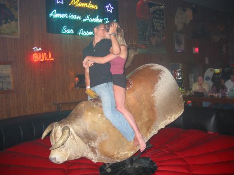 1989 Ford Bronco - A couple rides a mechanical bull in a bar with neon signs in the background.