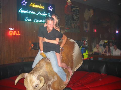1989 Ford Bronco - A couple enjoys a ride on a mechanical bull in a dimly lit bar with neon signs in the background.