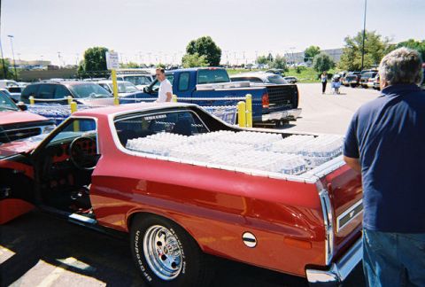 1972 Ford Ranchero - A red pickup truck is parked in a lot, its bed filled with cases of bottled water.