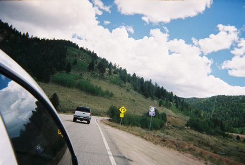 1972 Ford Ranchero - A white pickup truck travels along a scenic mountain highway, passing by road signs and dense evergreen forests.