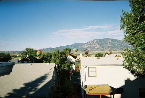 1972 Ford Ranchero - Hot air balloons drift across a clear blue sky above houses and trees, with a mountain range visible in the distance.