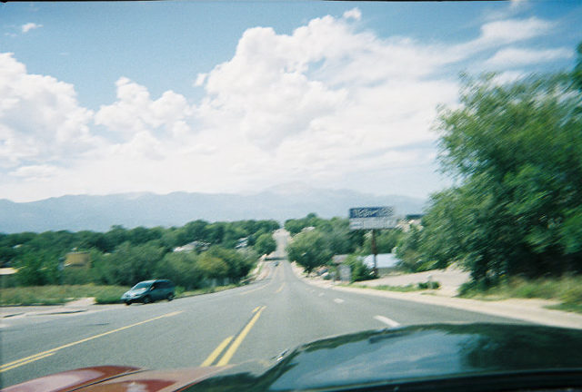Red car dashboard in foreground, driving on a road with a blue car visible on the left
