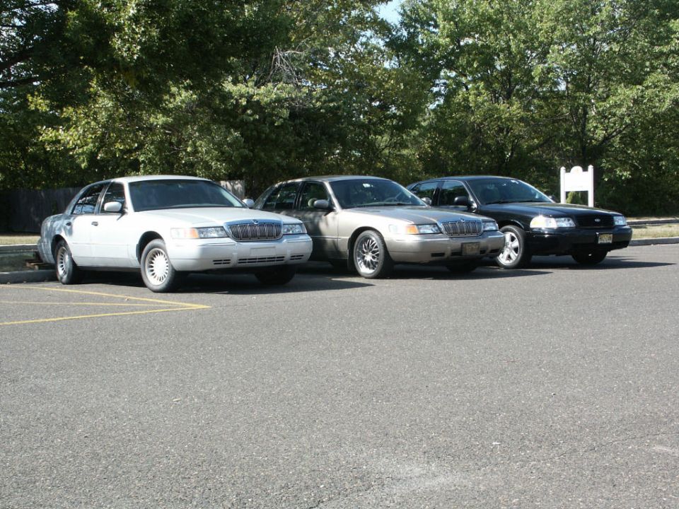 Three full-size sedans parked in a row: white Lincoln, silver Mercury and black Crown Victoria