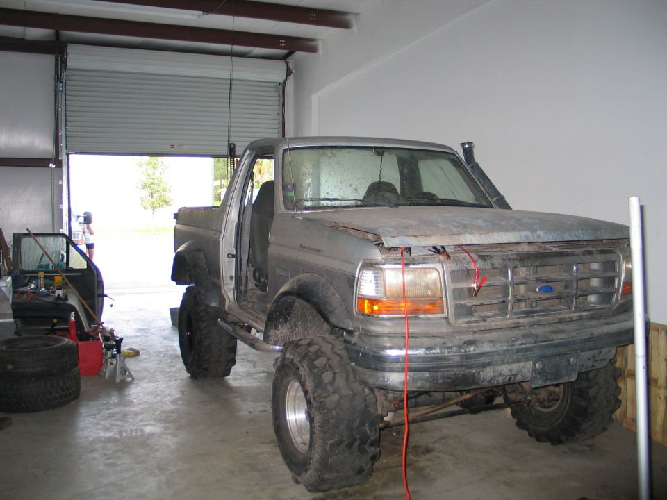 Lifted Ford F-series pickup on large mud tires inside a metal shop, primered fenders