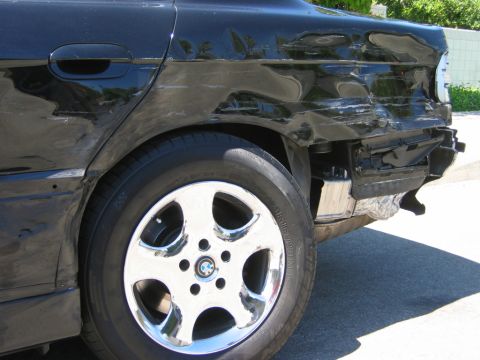1985 Ford Bronco - Rear view of a damaged black sedan, showing crumpled bodywork and exposed internal components.
