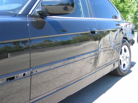 1985 Ford Bronco - This black sedan shows extensive damage to its side, including the rear quarter panel and door, indicating a significant impact.