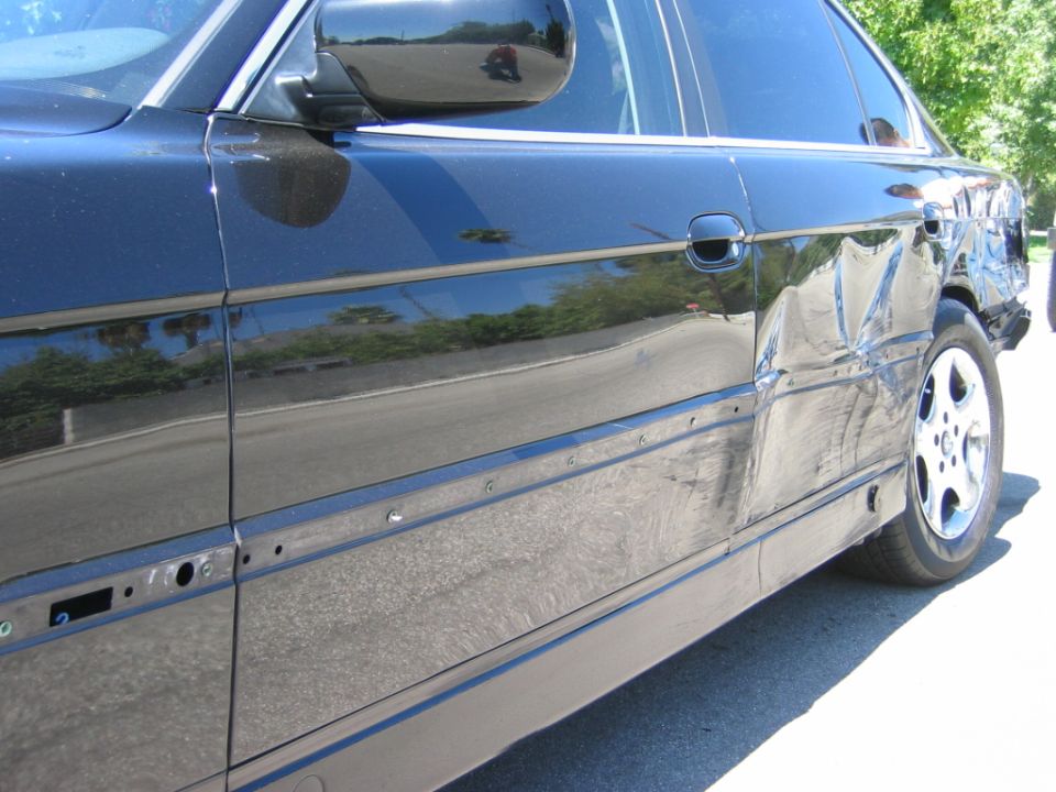 Dented rear door and quarter panel on a black sedan with side trim removed