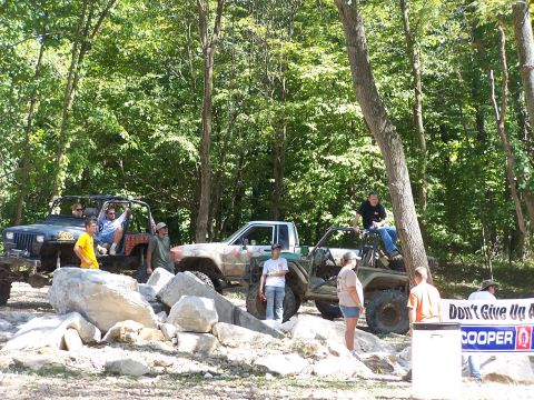 1992 Ford Bronco - A group of people and their off-road vehicles gather in a wooded area with rocky terrain.