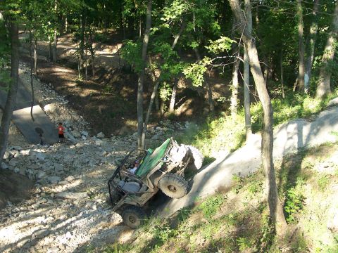 1992 Ford Bronco - An off-road vehicle attempts to climb a steep, rocky incline in a forest.