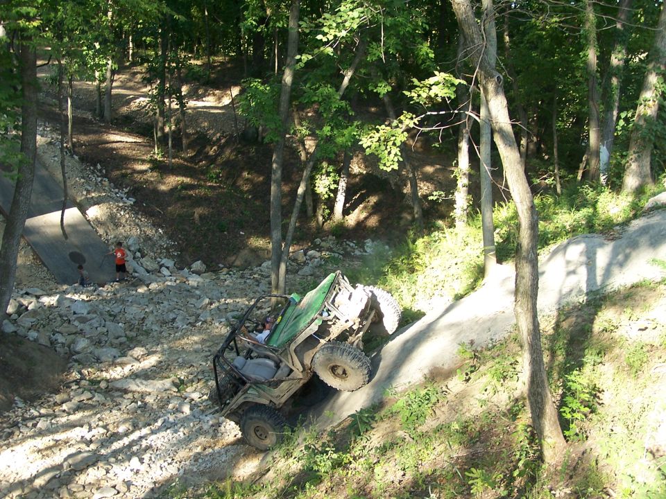 Off-road vehicle with roll cage navigating a steep, rocky trail in a wooded area