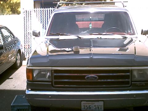 1990 Ford Bronco - Front view of a 1990 Ford Bronco, showing the grille and Ford emblem. A second vehicle is visible to the left.
