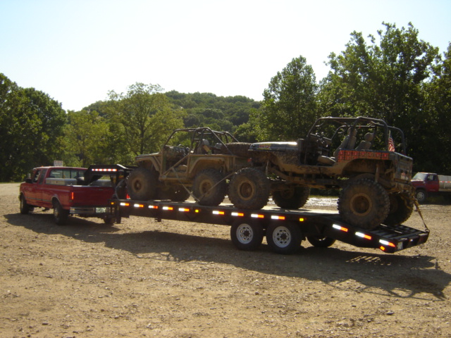 Red pickup truck towing trailer with two off-road vehicles