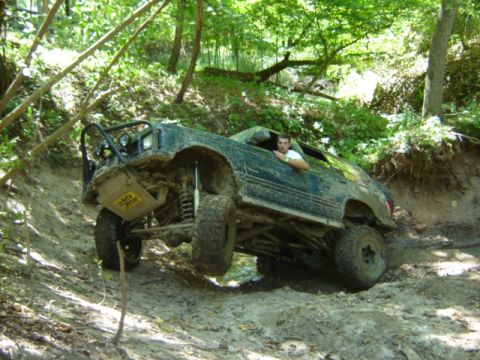 1992 Ford Bronco - A 1992 Ford Bronco navigates a steep, muddy incline in a wooded area.