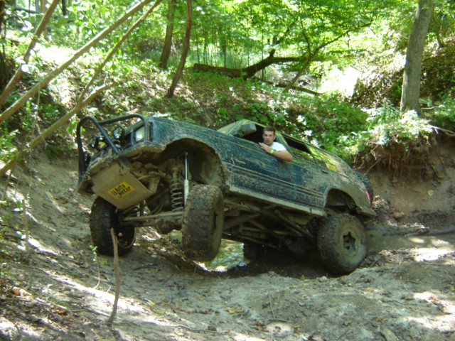 Dark green 1992 Ford Bronco off-roading on a muddy hill, driver visible