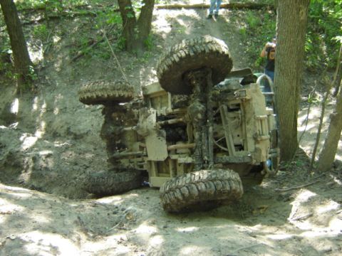 1992 Ford Bronco - An off-road vehicle has overturned on a muddy embankment, its tires pointing skyward.