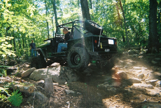Black off-road vehicle with a roll cage and spare tire on the back, navigating a rocky trail