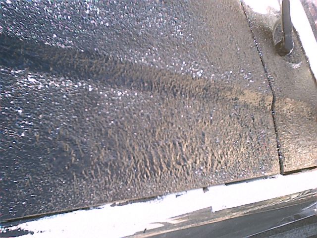 Close-up of a textured, peeling black painted panel with grayish oxidation and grit