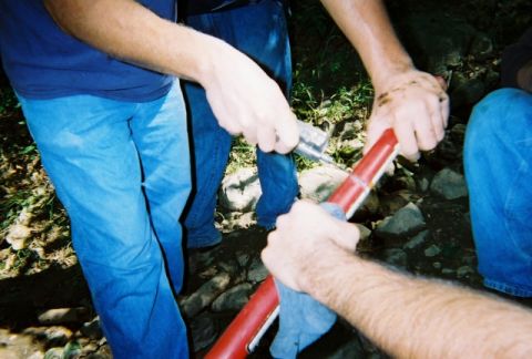 1976 GMC C/K Pickup - Several individuals are gathered outdoors, focused on manipulating a red and white cylindrical object with a tool.
