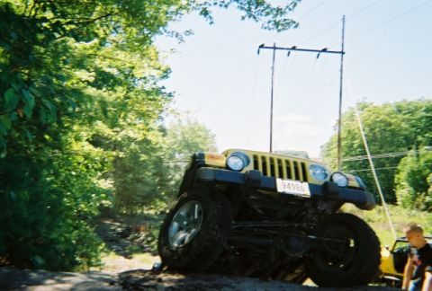 1976 GMC C/K Pickup - Jeep Wrangler navigating an off-road trail with trees and a utility pole in the background.