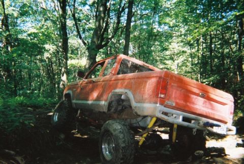 1976 GMC C/K Pickup - Modified pickup truck navigating a muddy, wooded path with large tires and lifted suspension.