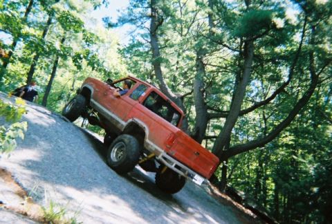 1976 GMC C/K Pickup - A modified pickup truck navigates a challenging off-road course on a sunny day.