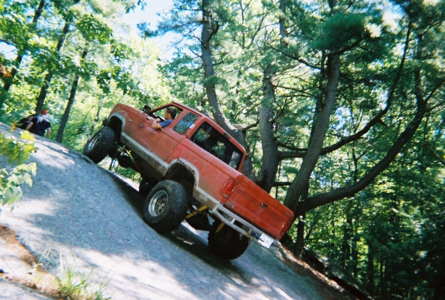 red pickup truck with large tires climbing a steep rock face, driver visible