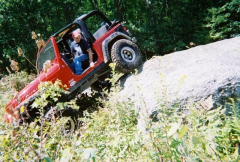 1976 GMC C/K Pickup - A red Jeep Wrangler Rubicon navigates a challenging rocky trail, demonstrating its off-road capabilities.