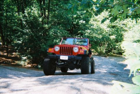 1976 GMC C/K Pickup - A red Jeep Wrangler is seen driving on a dirt path surrounded by trees.