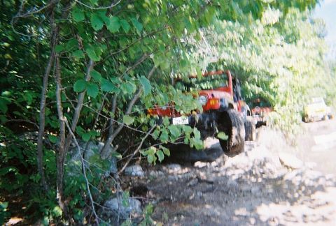 1976 GMC C/K Pickup - A red Jeep Wrangler navigates a challenging off-road course with another vehicle following.