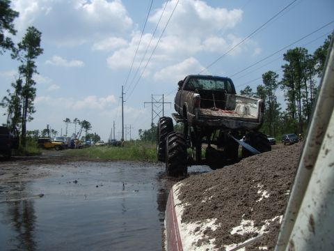 1978 Ford Bronco - A lifted pickup truck is stuck in a mud pit during an off-road event with other vehicles present.