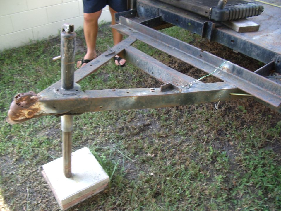 Trailer tongue with jack stand on concrete block, showing rusty coupler and metal frame