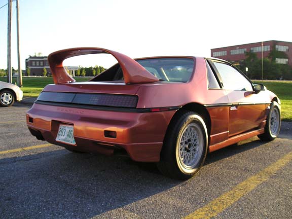 Red 1984 Pontiac Fiero with a large rear spoiler and aftermarket wheels parked on asphalt