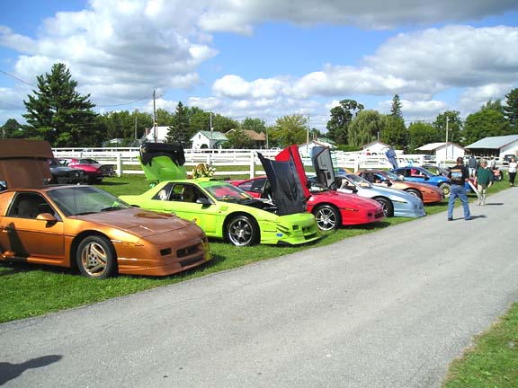 Several Pontiac Fieros parked in a row with hoods and doors open
