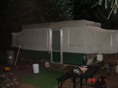1993 Ford Bronco - A pop-up tent trailer is set up at a campsite, with a table and lantern in the foreground.