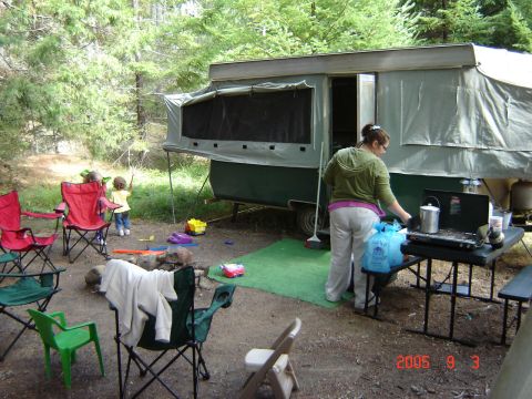 1993 Ford Bronco - A pop-up tent trailer is set up at a campsite, with camping chairs and a portable stove visible.