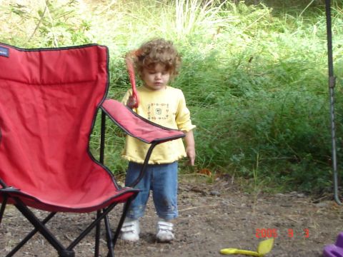1993 Ford Bronco - A child stands outdoors next to a red camping chair, holding a red brush.