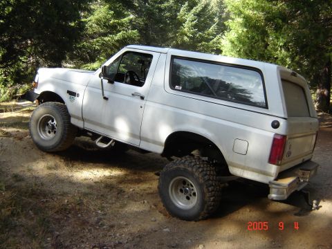 1993 Ford Bronco - White 1993 Ford Bronco driving on a dirt path surrounded by trees.