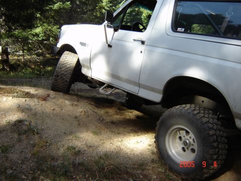 1993 Ford Bronco - White SUV with large tires navigating rough terrain, showing its side profile.