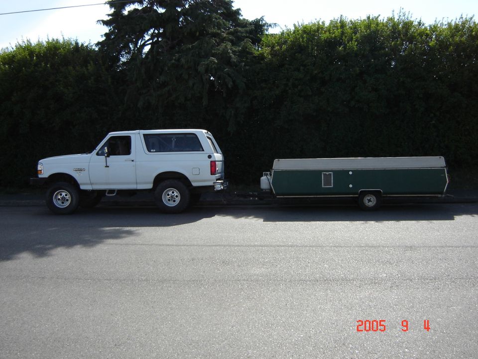 White 1993 Ford Bronco parked next to a green pop-up camper on a street