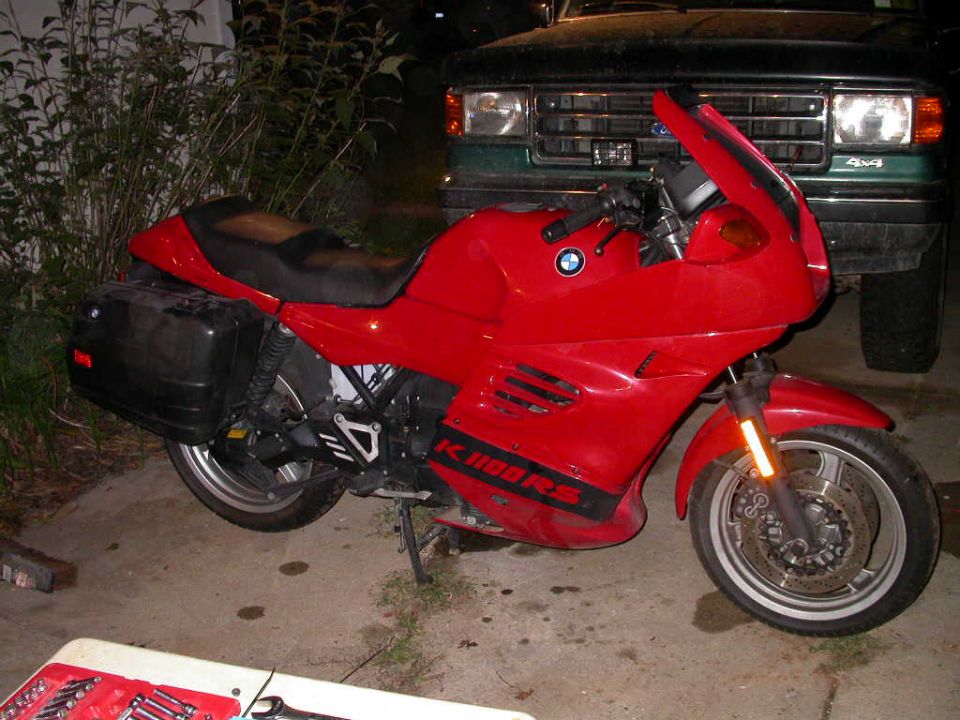Red BMW K-series sport-touring motorcycle with hard saddlebag parked beside a green truck