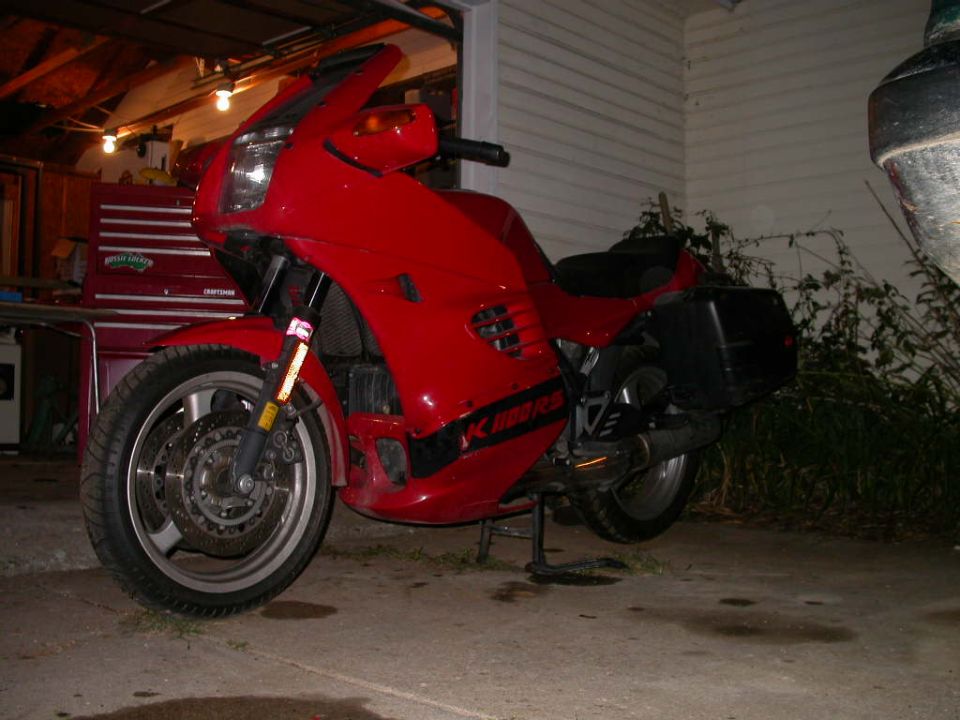 Red BMW K-series motorcycle with saddlebags parked in front of an open garage at night