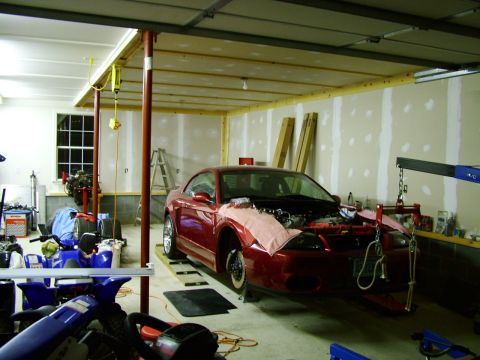 2003 Ford Mustang - A red 2003 Ford Mustang coupe is parked in a garage with its hood open, undergoing maintenance.