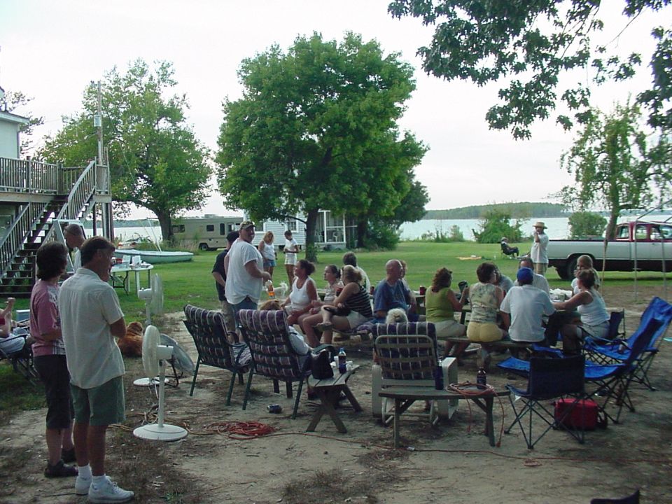 People gathered outside by a lake, with an RV and a pickup truck visible