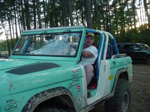 1969 Ford Bronco - Man sits in a modified teal first-generation Ford Bronco with a roll cage and racing decals.