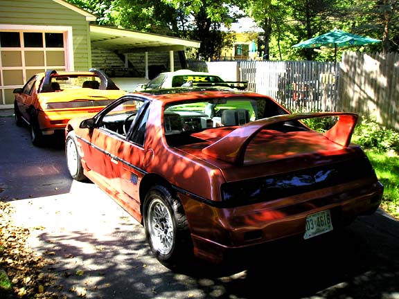 Red 1984 Pontiac Fiero, rear view, with large spoiler and yellow Fiero behind it