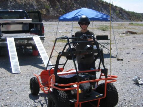 1994 Ford Bronco - A person in a helmet stands by an orange go-kart next to a pickup truck with ramps.