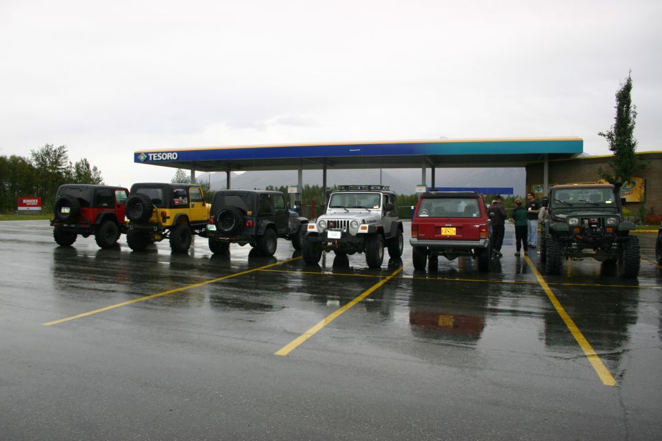 Several Jeeps parked in a line at a Tesoro gas station under a cloudy sky